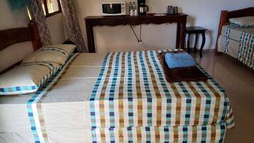 A bedroom with two beds, a wooden headboard, a bedside table with a microwave, a coffee maker, and a small table.