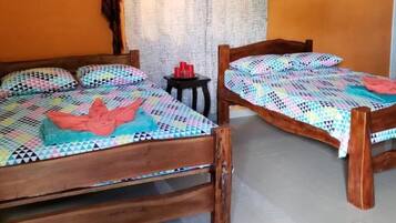 Due letti di legno con coperte e asciugamani colorati, un tavolino con bicchieri rossi e una tenda sullo sfondo.