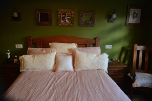 Uma cama bem arrumada com colcha xadrez e várias almofadas, cabeceira de madeira e mesa de cabeceira com abajur e uma pequena moldura.