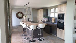 Una cocina moderna con una isla central, taburetes de bar, horno empotrado y un ventanal grande.