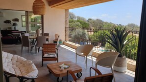 Un balcón con asientos, zona de comedor y vista a una piscina y follaje.