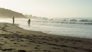 Una playa con huellas que conducen al agua, un cielo despejado y una costa distante.