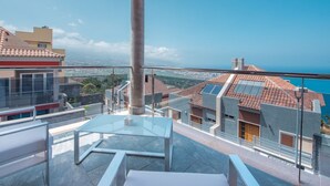 Un balcón con una mesa y sillas de vidrio, que ofrece vistas a la ciudad y al mar.