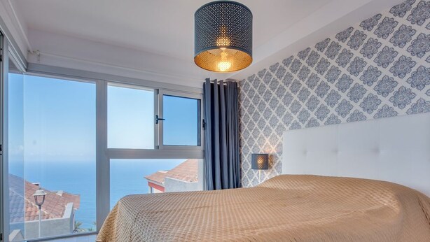 Un dormitorio con una cama grande, vista al mar y un papel tapiz estampado.