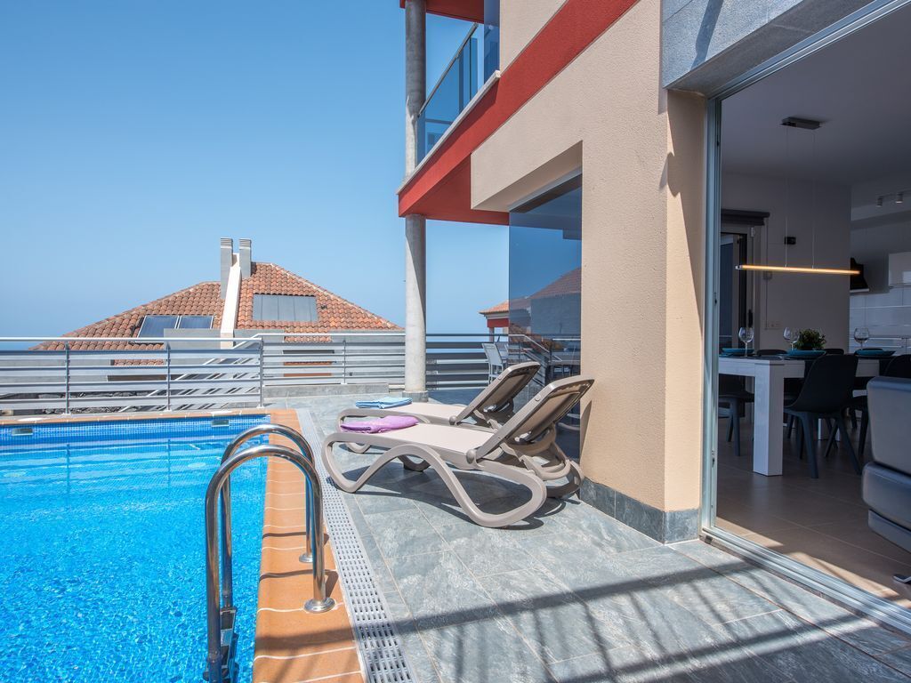 A poolside area with lounge chairs, a pool, and a view of a building with a red roof.
