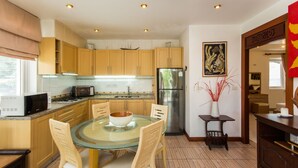 A modern kitchen with wooden cabinets, a glass dining table, and a stainless steel refrigerator. - Magical, 2 Bedroom Apartment in Beachside Complex (Koh Samui)