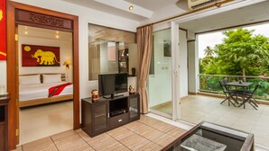A modern hotel room with a television on a dark wooden cabinet, a bed with a red blanket, and a balcony with a table and chairs. - Magical, 2 Bedroom Apartment in Beachside Complex (Koh Samui)