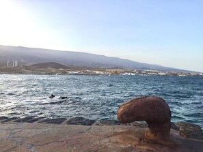 A coastal view with a rocky foreground, a calm sea, and a distant town with buildings and wind turbines. - BALCONY TO THE SEA, HOLIDAY APARTMENT - PORÍS 8 (Porís de Abona)