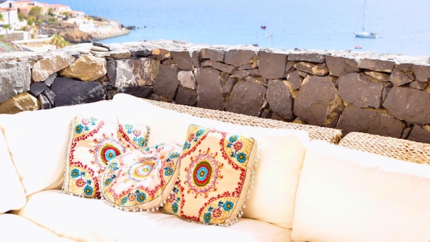 A stone wall with a woven sofa and colorful cushions, overlooking a coastal area with buildings and boats. - BALCONY TO THE SEA, HOLIDAY APARTMENT - PORÍS 8 (Porís de Abona)
