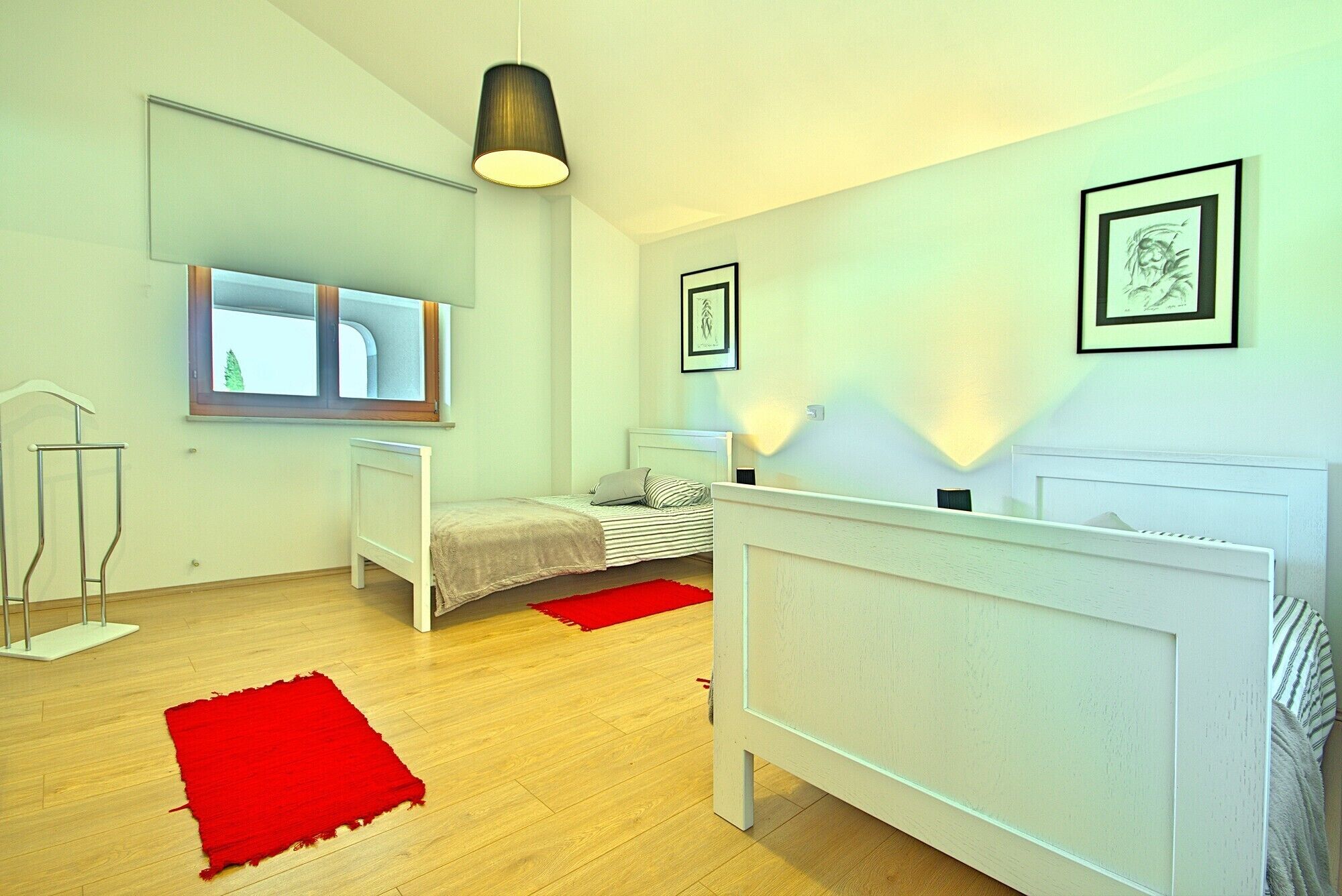 A modern bedroom with a large bed, a smaller bed, a mirror, and a red rug.