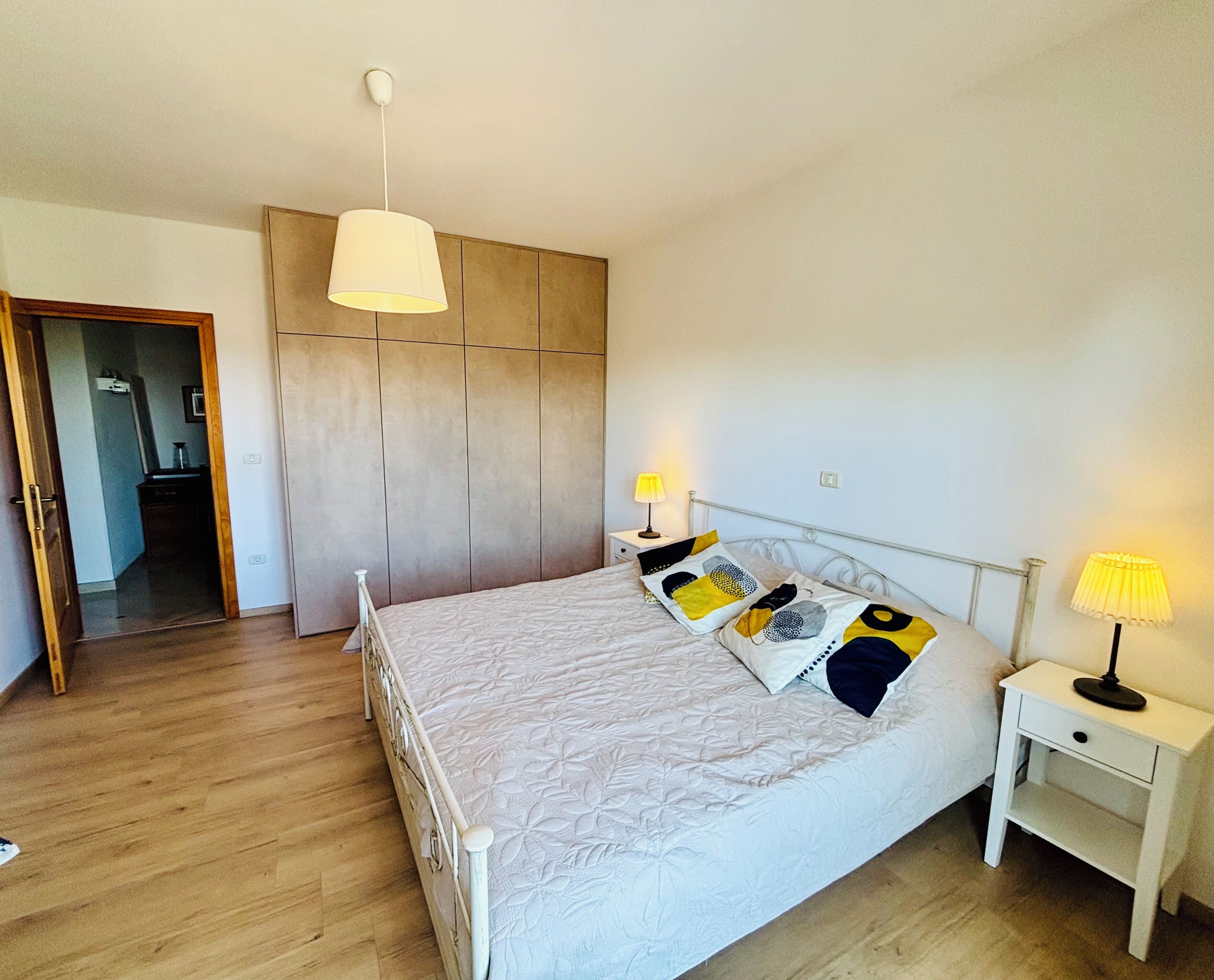 Une chambre à coucher comprenant un lit, des tables de chevet, une lampe suspendue et une armoire.