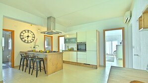 Une cuisine moderne dotée d’un îlot central, de tabourets de bar, d’une grande horloge murale et d’un four encastré.