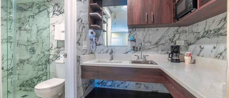 A modern bathroom with a glass-enclosed shower, a toilet, a sink with a vanity, and a microwave above the counter.