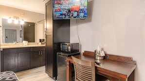 A compact hotel room with a kitchenette, a microwave, a coffee maker, a TV mounted on the wall, and a wooden dining table with a chair. - Sunshine Inn (Kissimmee)