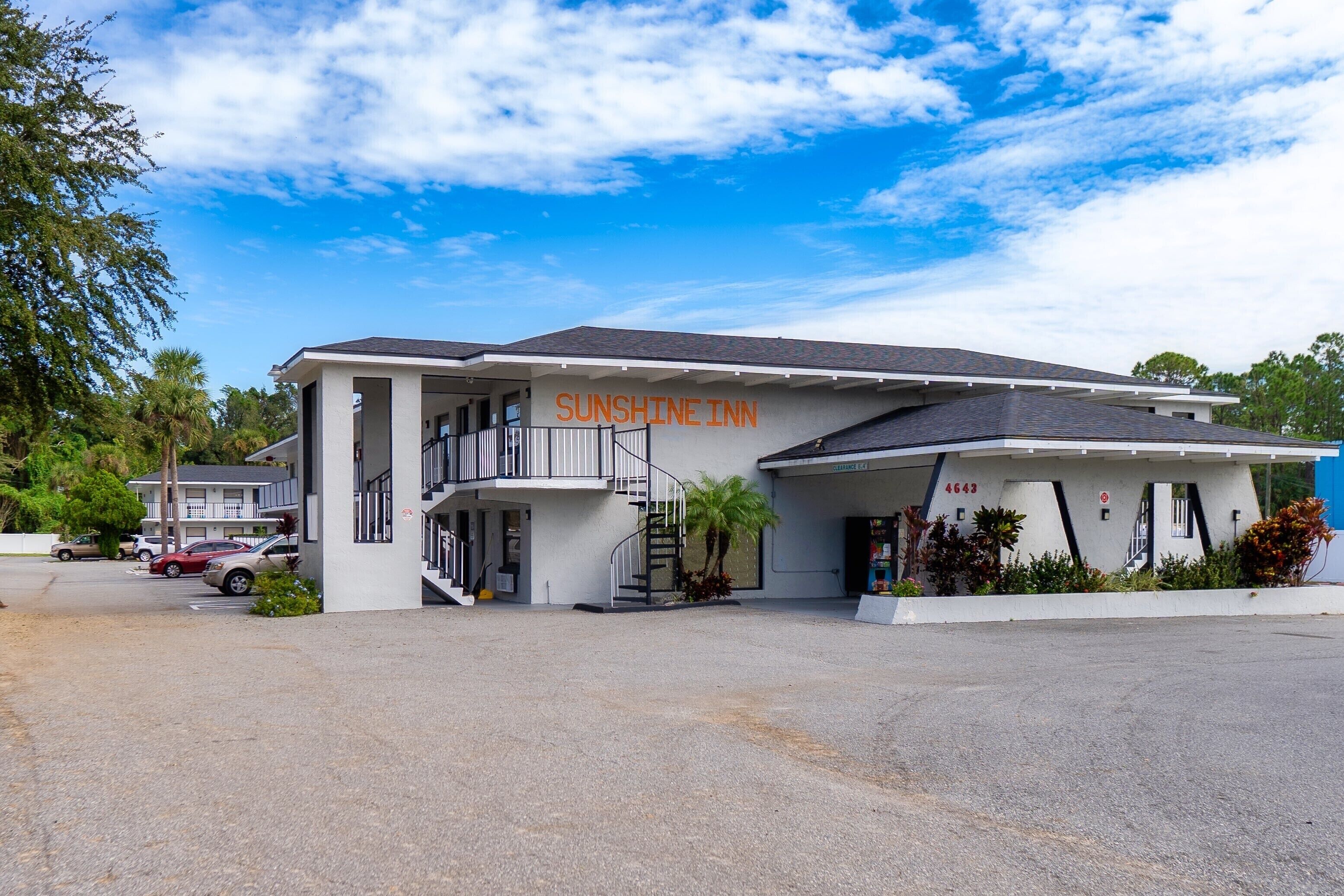 Un motel à deux étages appelé Sunshine Inn, avec un parking situé devant.