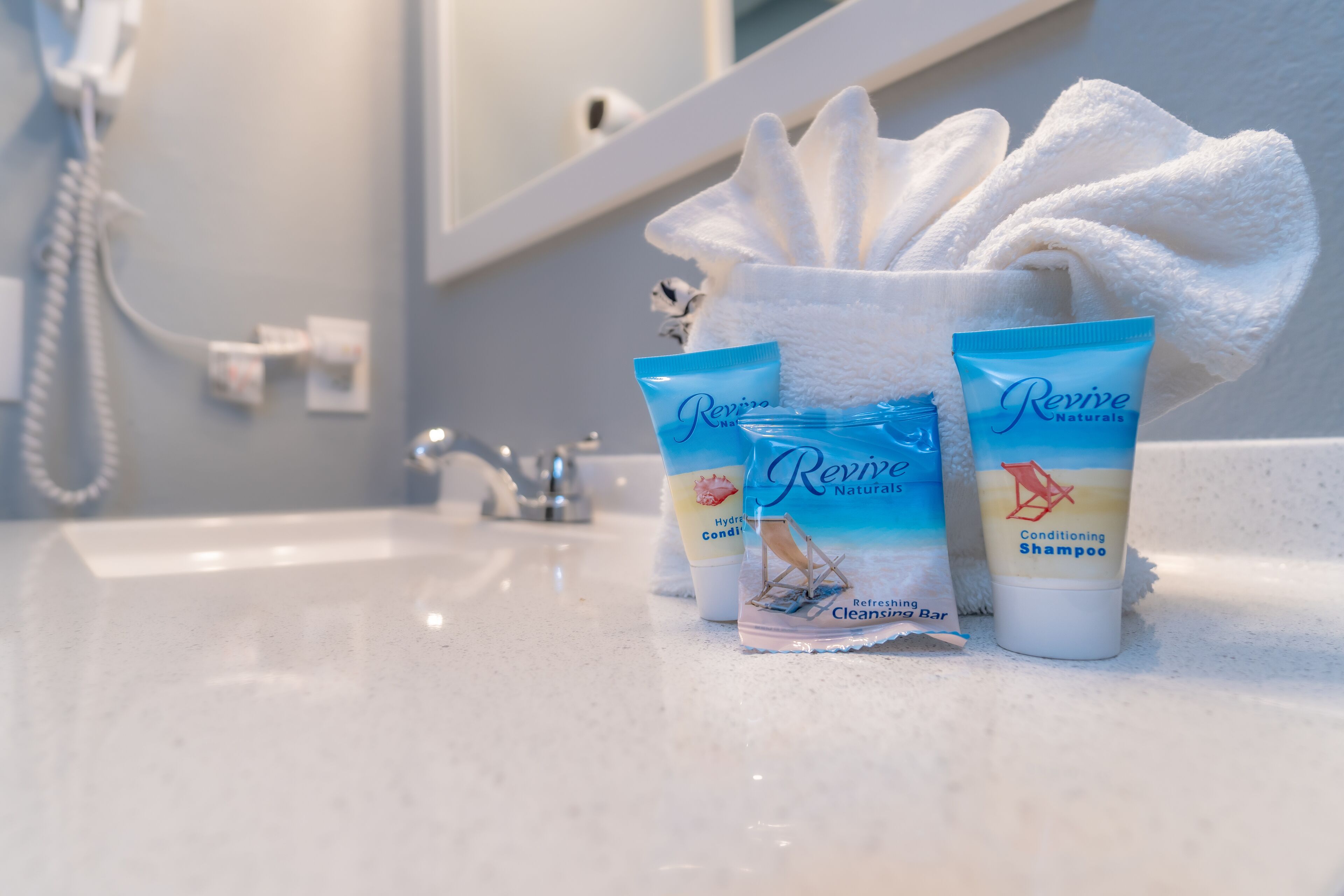 A bathroom sink with toiletries including a hydrating conditioner, a refreshing cleansing bar, and conditioning shampoo.
