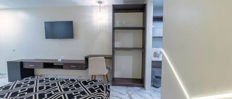 A hotel room with a bed, a desk, a chair, a TV, and a wardrobe.