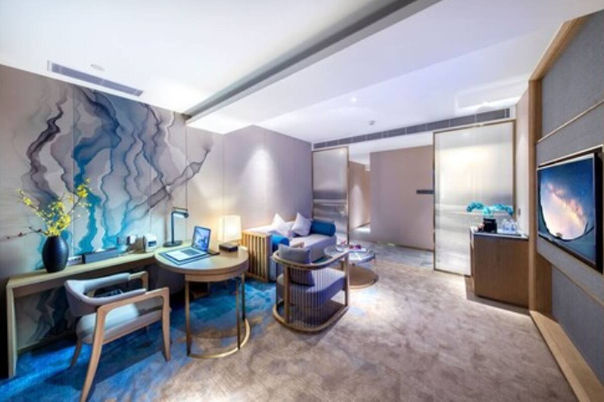A modern hotel room with a desk, seating area, and a large TV.