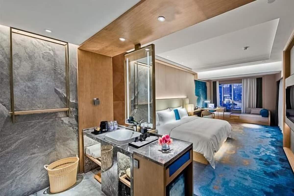 A modern hotel room with a marble bathroom, a large bed, a sitting area with a view, and a flat-screen TV.