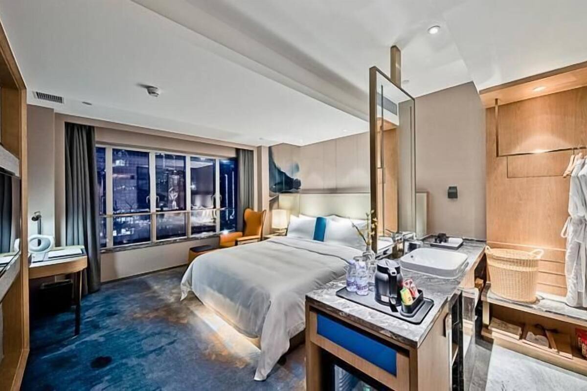A hotel room with a bed, a desk, a bathroom with a sink and mirror, and a view of the city at night.