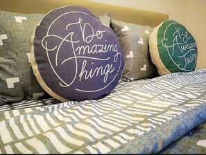 A bed with patterned bedding and two decorative pillows with motivational phrases.