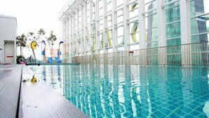 Ein Schwimmbecken mit klarem Wasser, umgeben von einem weißen Gebäude mit großen Fenstern.