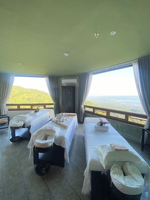A room with two beds, a massage table, and a view of a green landscape. - Alta D' Tagaytay Hotel (Tagaytay)
