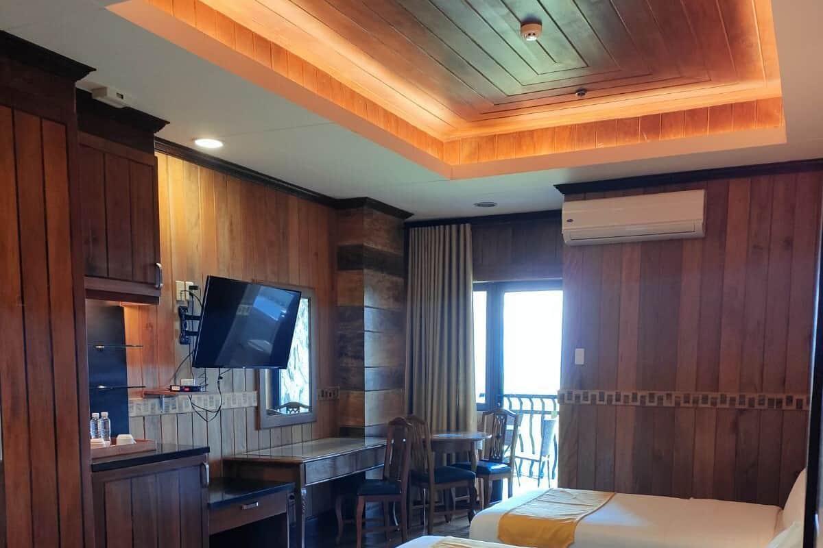 A hotel room with two beds, a desk with a TV, and a balcony.