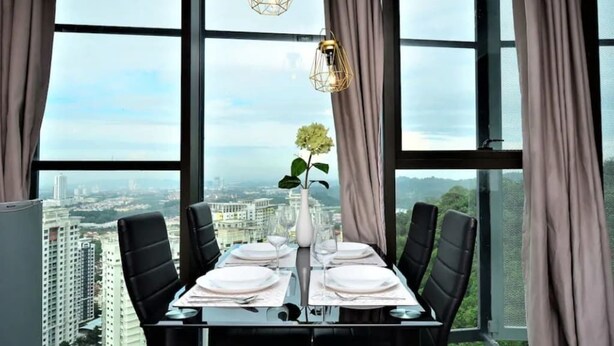 A dining table set for four with a vase of flowers, two pendant lights, and a city view through large windows. - 5 Pax Empire Soho by SYNC (Petaling Jaya)