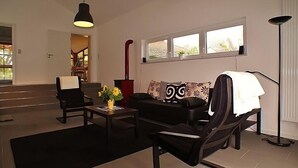 A modern living room with a sofa, armchairs, a coffee table, and a floor lamp. There is a window with a view of the outside.
