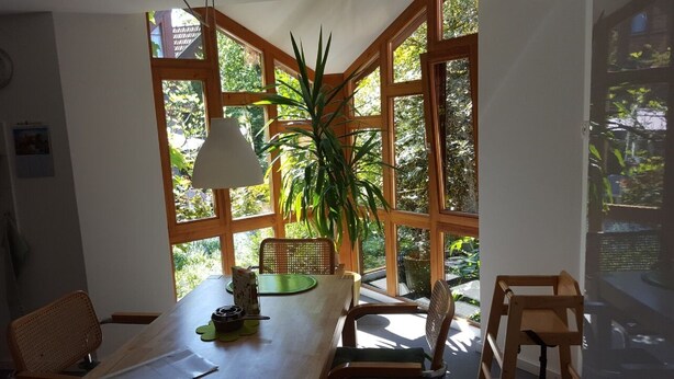 A dining area with a wooden table, chairs, and a large window with a plant in the center.