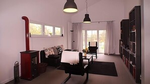 A modern living room with a fireplace, a black sofa, a dining table with chairs, and a bookshelf.