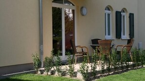 Un patio con sillas de mimbre, una mesa, un vidrio y una pequeña zona ajardinada.