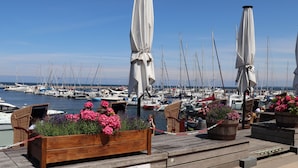 Un puerto deportivo con barcos amarrados, macetas de madera con flores y sombrillas blancas.