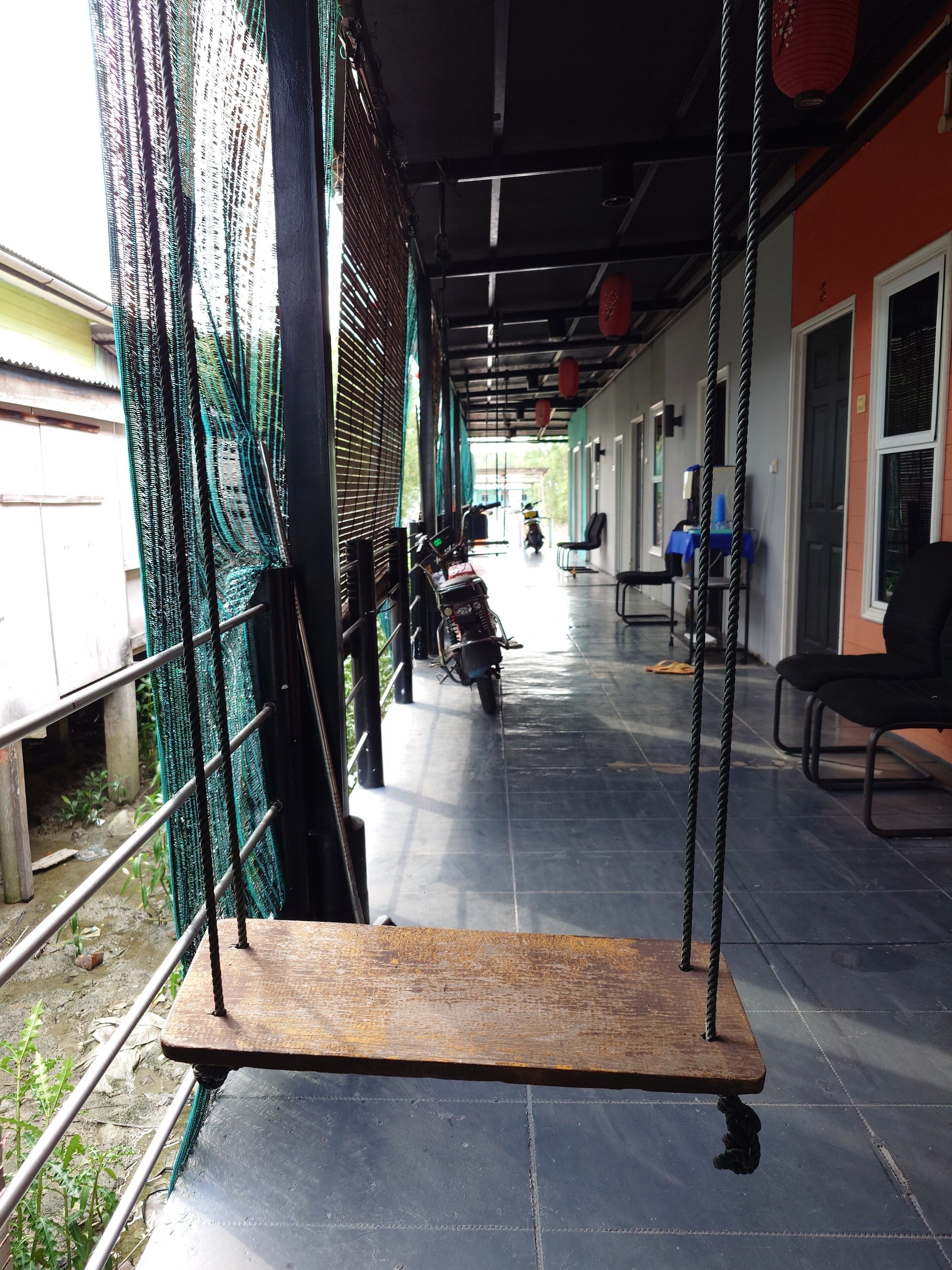 A covered outdoor area with a swing, a motorcycle, and a row of chairs.