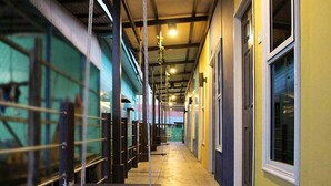 Um corredor com guarda-corpos de metal, piso de concreto e parede amarela com uma janela.