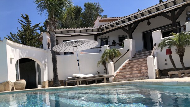 Una piscina cristallina con un ombrellone, una scala e un edificio bianco con tetto in tegole.