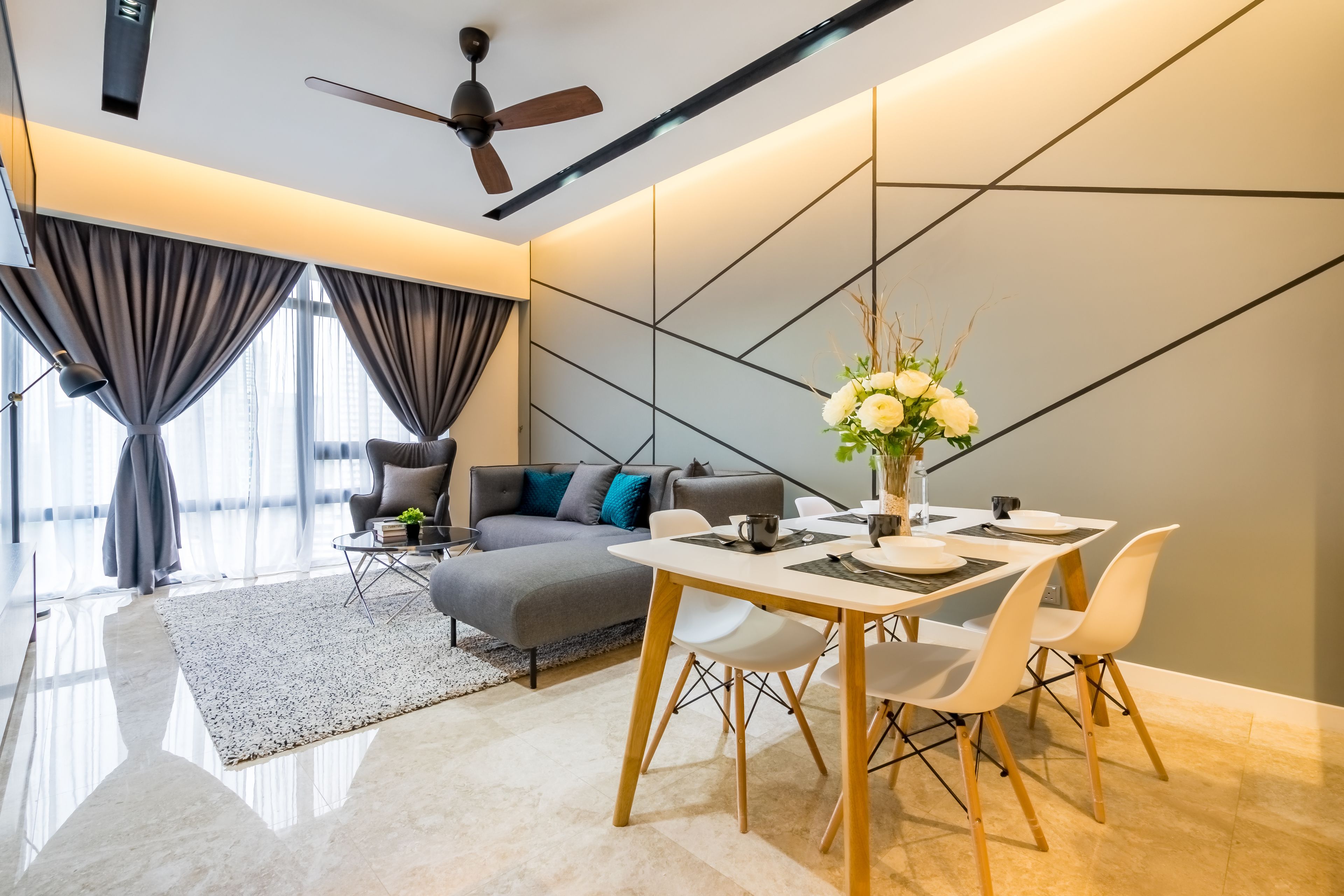 Ein modernes Wohnzimmer mit Sofa, Esstisch und Stühlen. Eine Deckenleuchte, eine Vase mit Blumen und ein großes Fenster mit Vorhängen sind ebenfalls vorhanden.