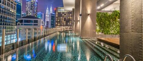 Ein moderner, überdachter Pool mit Blick auf die Stadt, ausgestattet mit einer Glasscheibe und einer grünen Wand.