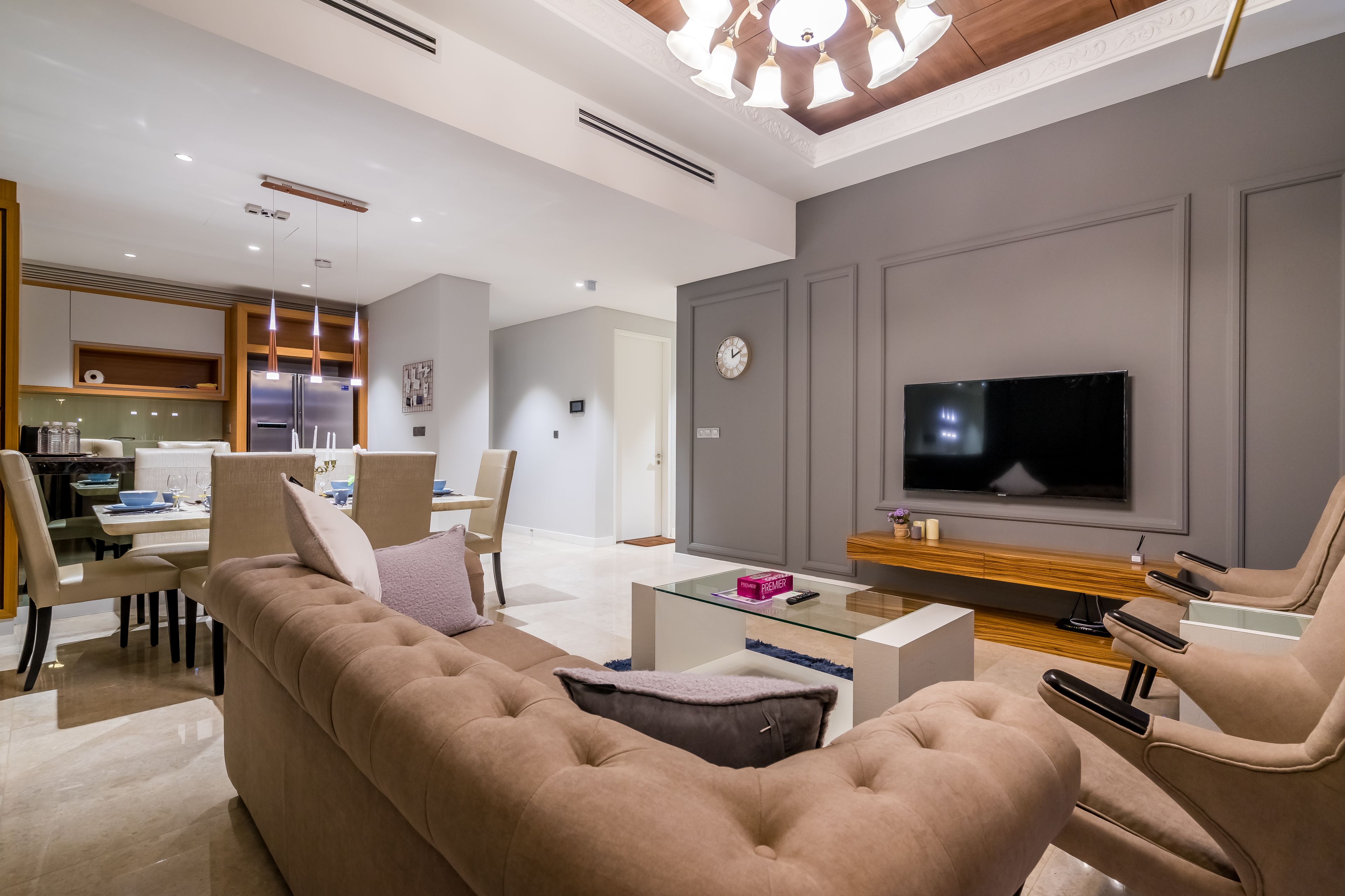 A modern living room with a large TV, comfortable seating, and a kitchen area in the background.