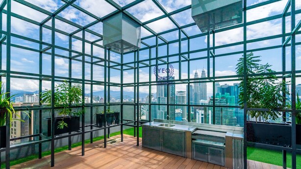 A modern glass-enclosed balcony with a wooden floor, city skyline views, and potted plants. - Anggun Residences Serviced Suites (Kuala Lumpur)