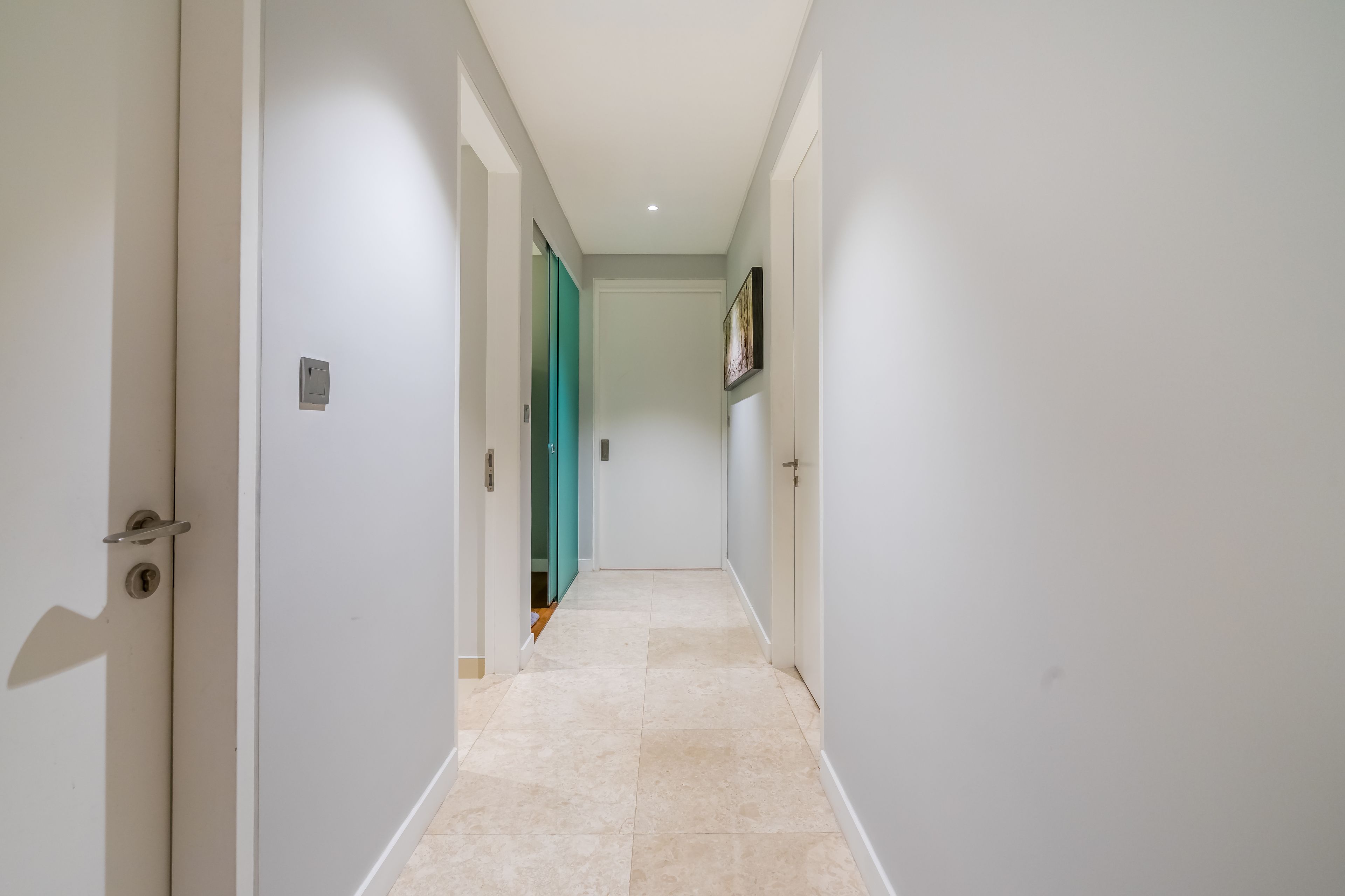 A narrow hallway with white walls and a tiled floor, leading to a door with a green frame.