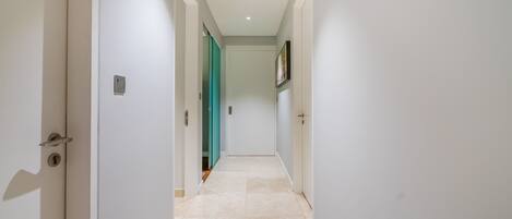 A narrow hallway with white walls and a tiled floor, leading to a door with a green frame.