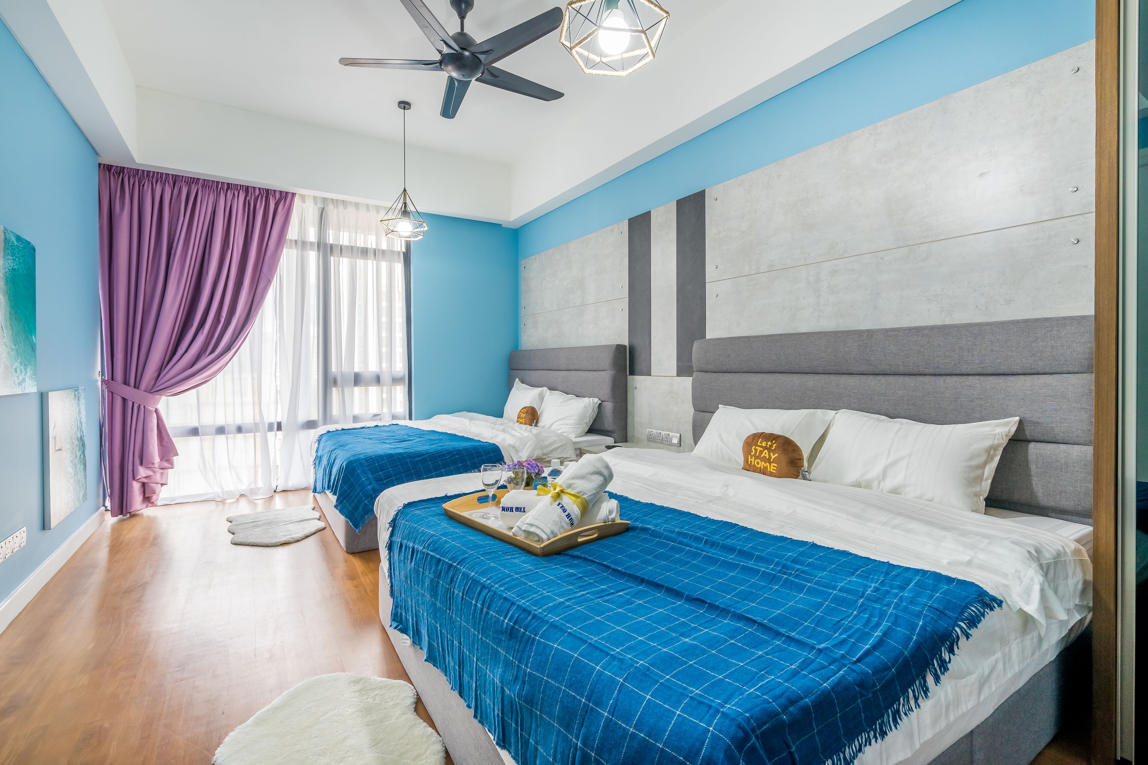 Ein modernes Hotelzimmer mit zwei Betten, einem Deckenventilator und einem großen Fenster mit violetten Vorhängen.