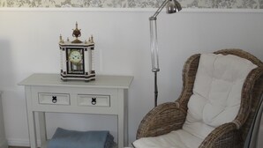 Ein Eckzimmer mit einem weißen Schreibtisch, einem Korbstuhl mit Kissen, einer blauen Tagesdecke und einer Stehlampe.