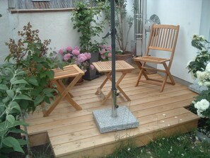 A wooden deck with two wooden chairs and a table, surrounded by potted plants and flowers. - Cottage apartment in Caputh-Schwielowsee with Havel view (Caputh)