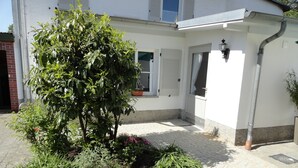 Ein Innenhof mit Baum, Blumenbeet und Gebäude mit weißer Fassade und einer Tür.