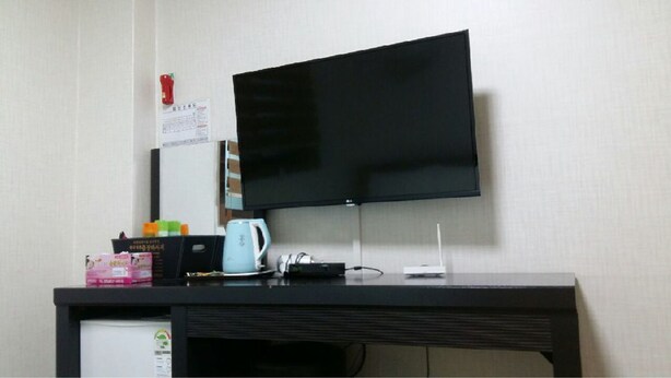 A hotel room with a flat-screen TV mounted on the wall, a small desk with a kettle, a coffee maker, and some items on it. - Booyoung Motel (Geoje)