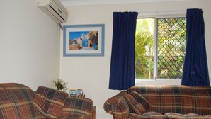 A living room with two plaid sofas, a framed picture on the wall, and a window with blue curtains. - Manly Peninsular (Wynnum)