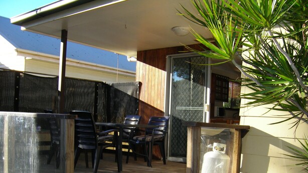 A covered outdoor patio with a table and chairs, a glass enclosure, and a potted plant. - Manly Peninsular (Wynnum)